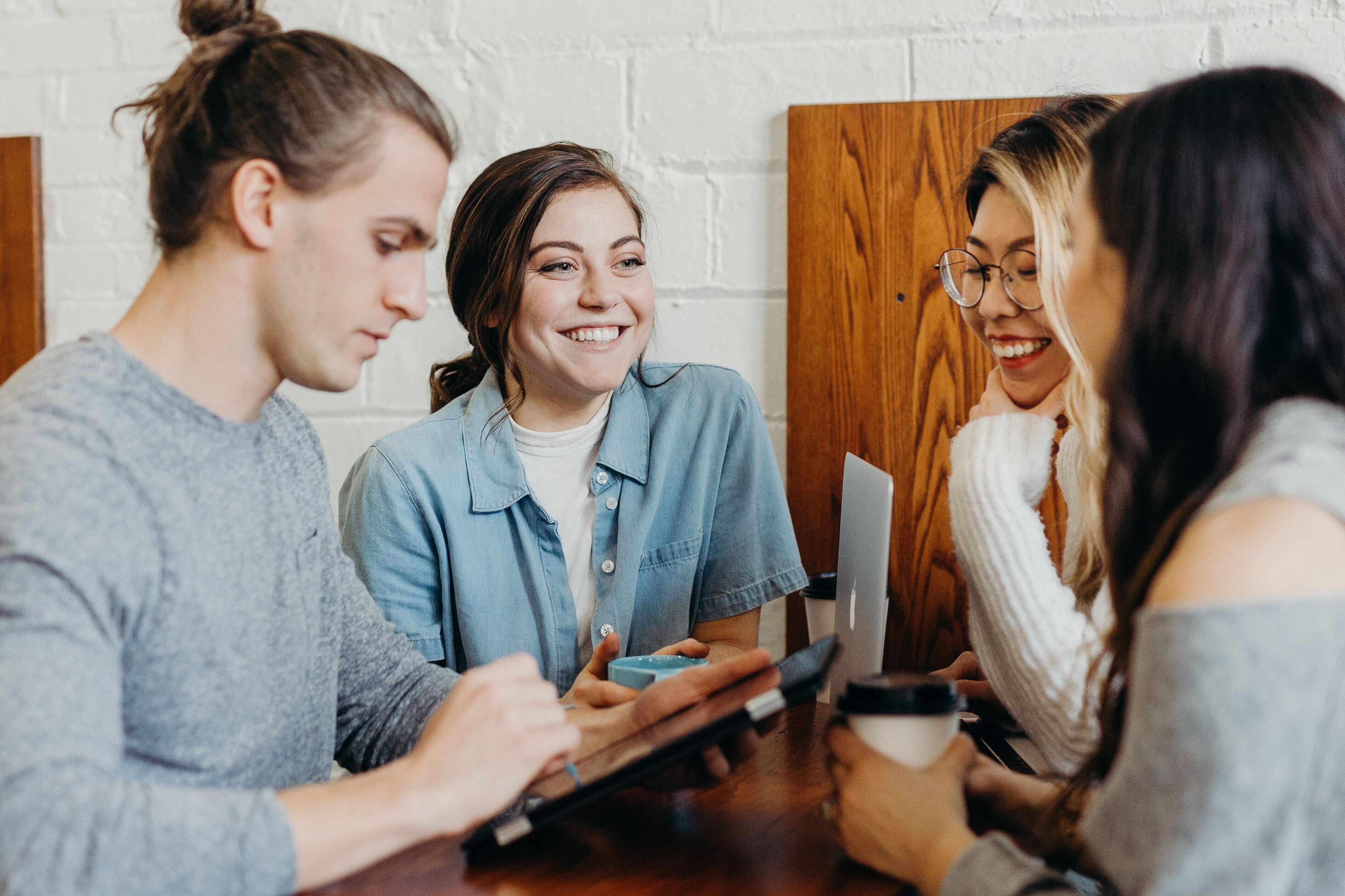 Smiling group of young adults on smart devices at coffee shop